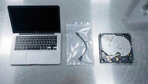 A laptop, a sealed evidence bag and a labelled hard drive arranged on a clean examination bench.