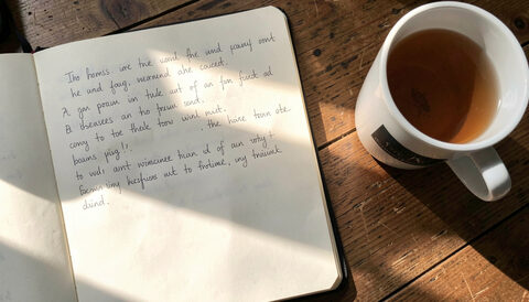 A single open notebook of handwritten definitions on a desk beside a mug of tea in morning light.
